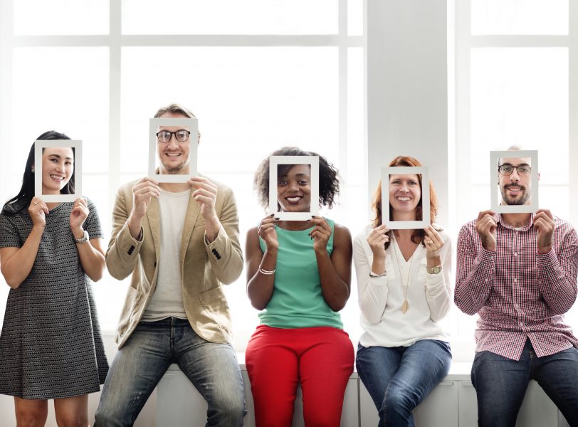 5 diverse smiling people holding a square frame up to their face - showing their face through the frame
